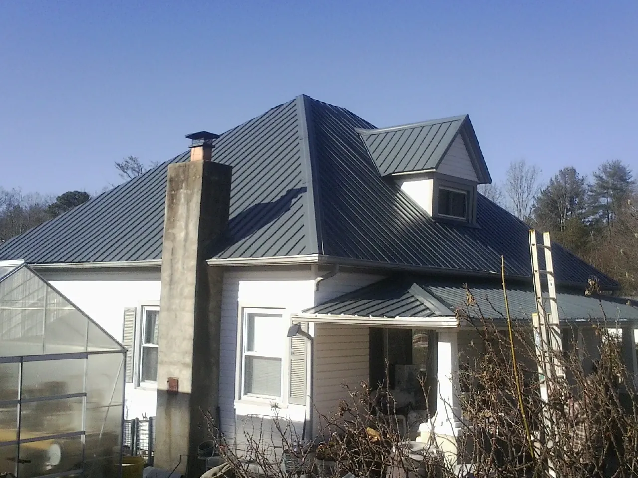 Dark blue standing seam metal roof on a white farmhouse with dormer — Slate & Tile Roof Repair by Roofing Brothers in West Finley