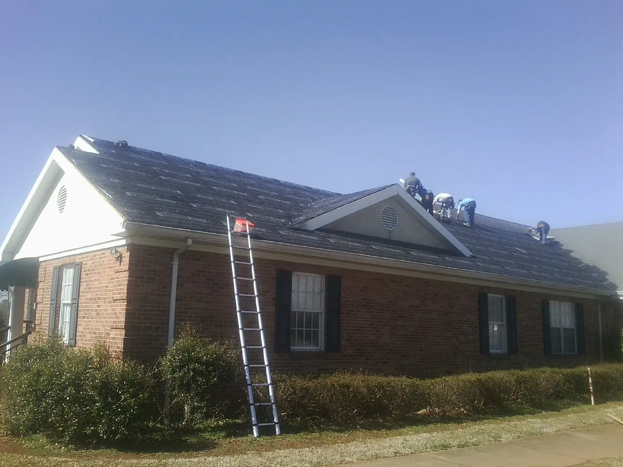 Crew tearing shingles off a brick ranch roof with a ladder set — Metal Roof Repair work by our crew in West Finley