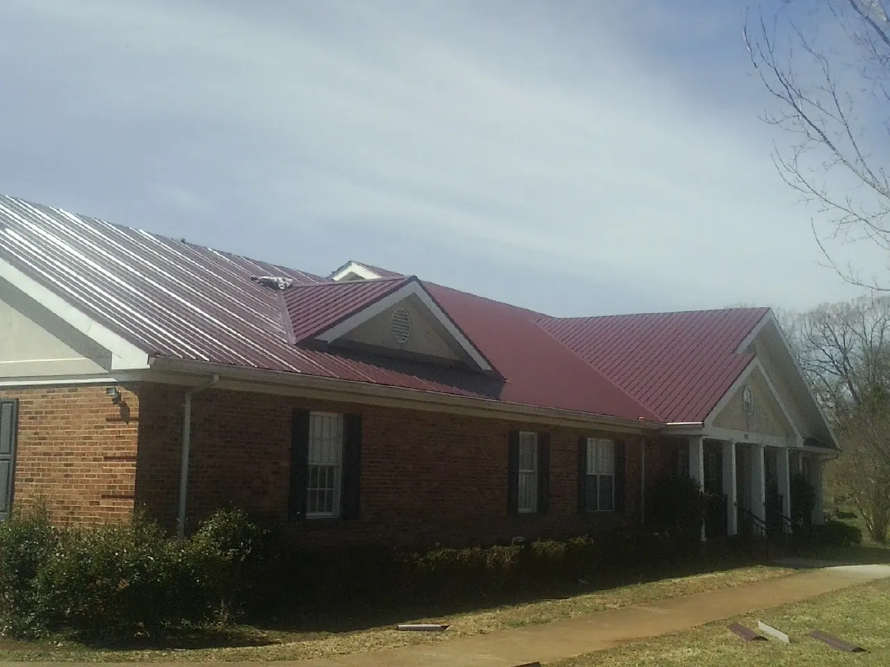 Red metal roof with gabled entries on a long brick building, from a Hail Damage Roof Repair job in West Finley