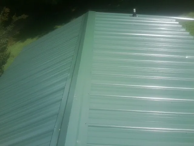 New green metal panels meeting at the ridge of a roof — Flat Roof Repair work by our crew in West Finley