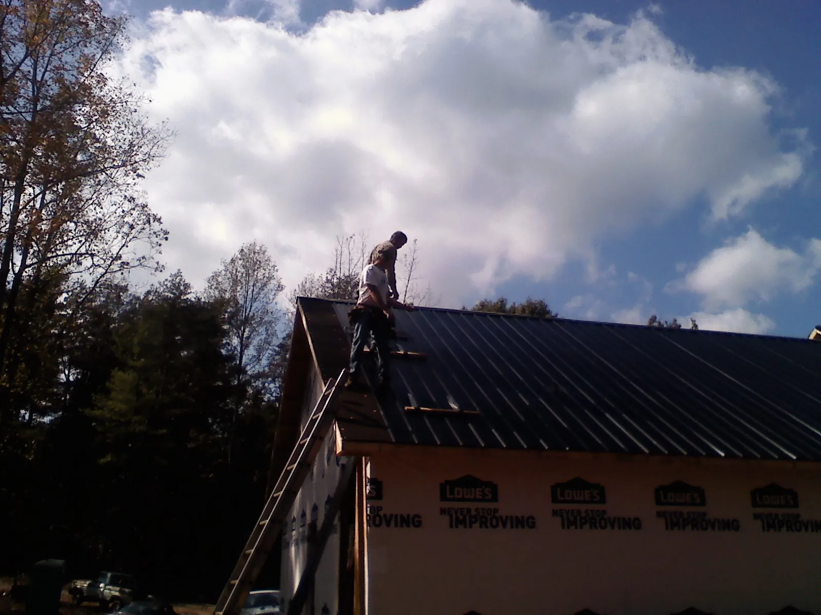 Roofer fastening dark metal panels high against a cloudy sky, from a Roof Inspection job in West Finley