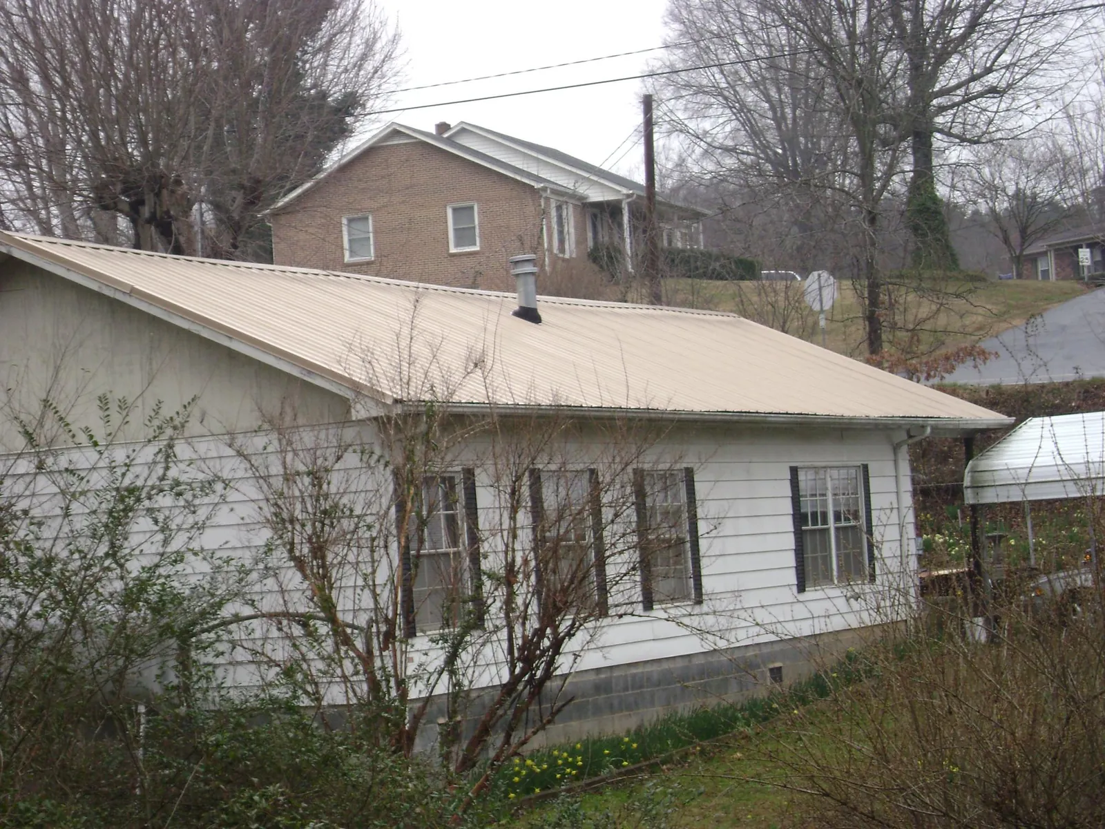 Tan metal roof on a white sided house set into a hillside — Commercial Roofing by Roofing Brothers in West Finley