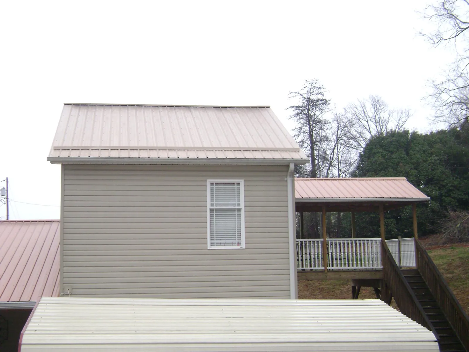 Tan metal roofs on a two story addition and attached porch, from a Roof Replacement job in West Finley